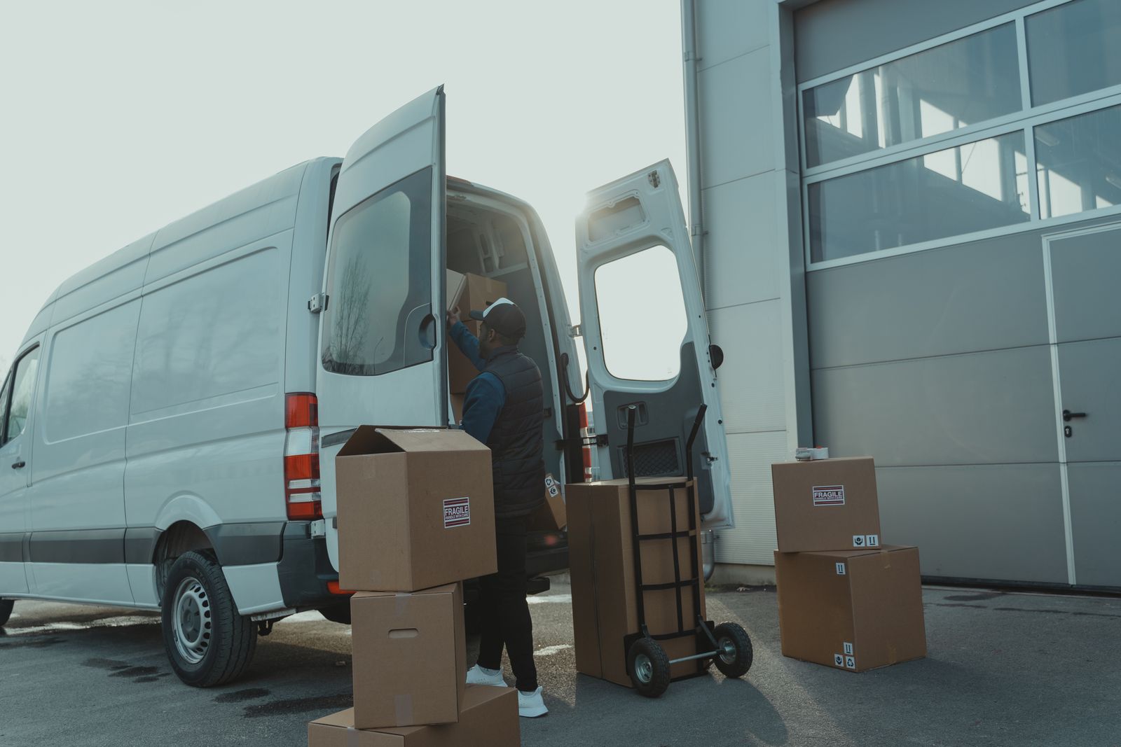 Courier loading cardboard boxes into a delivery van outside a warehouse